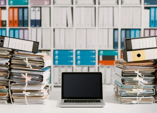 A Laptop in Between Two Piles of Documents